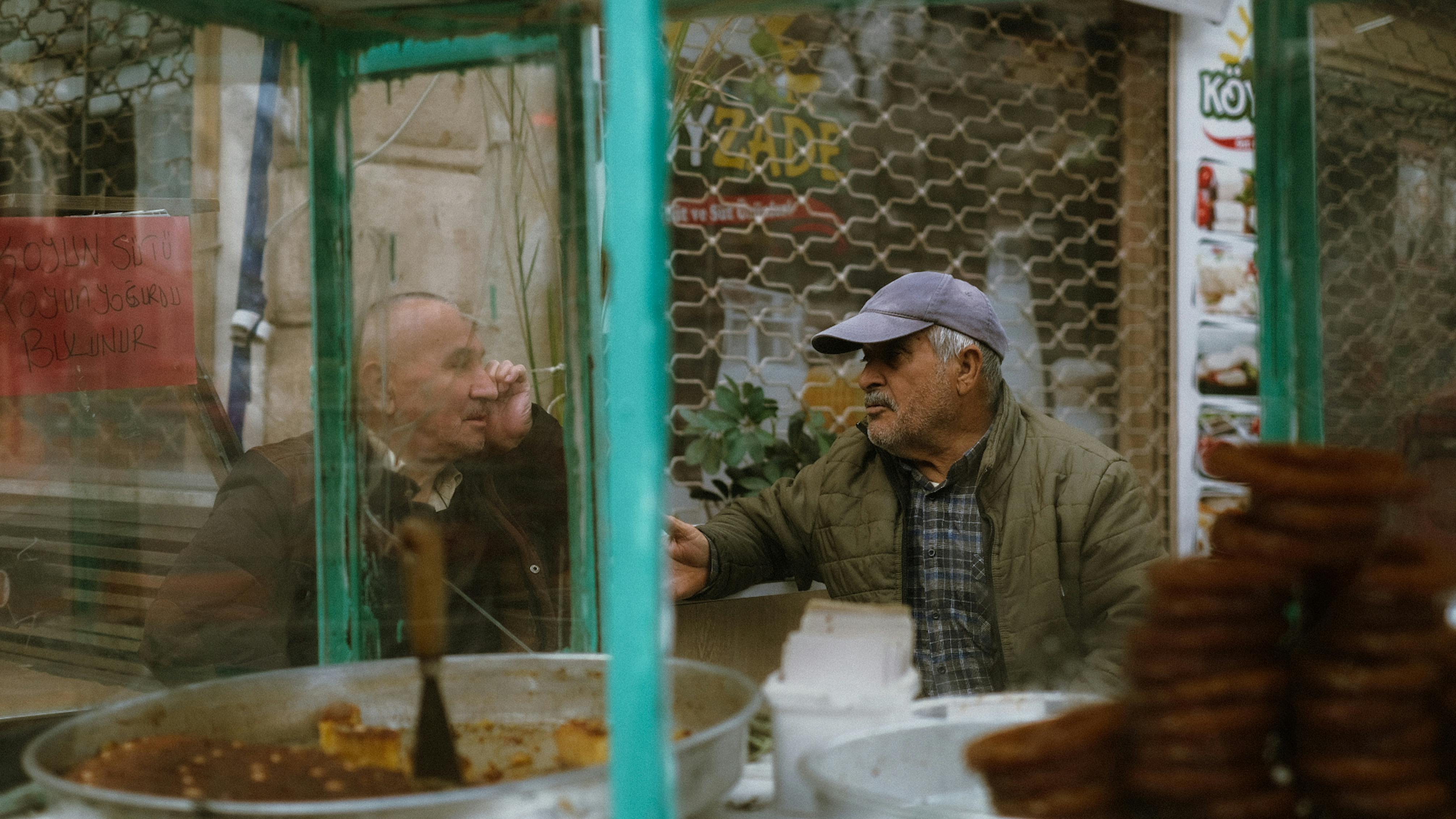two men sitting by a food stall and talking