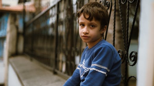 A young boy sitting on a bench in front of a fence