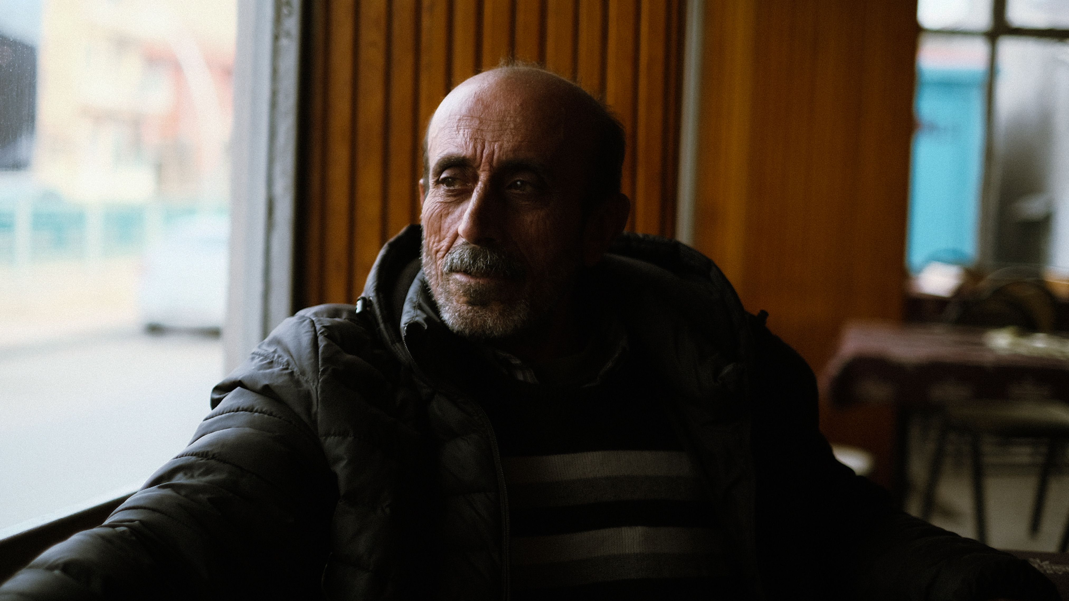 Emotive portrait of an elderly man seated in a cozy cafe, gazing thoughtfully out the window.