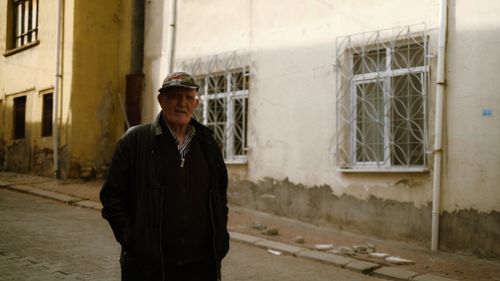 Free An elderly man wearing a cap and jacket stands in a quiet urban street. Stock Photo