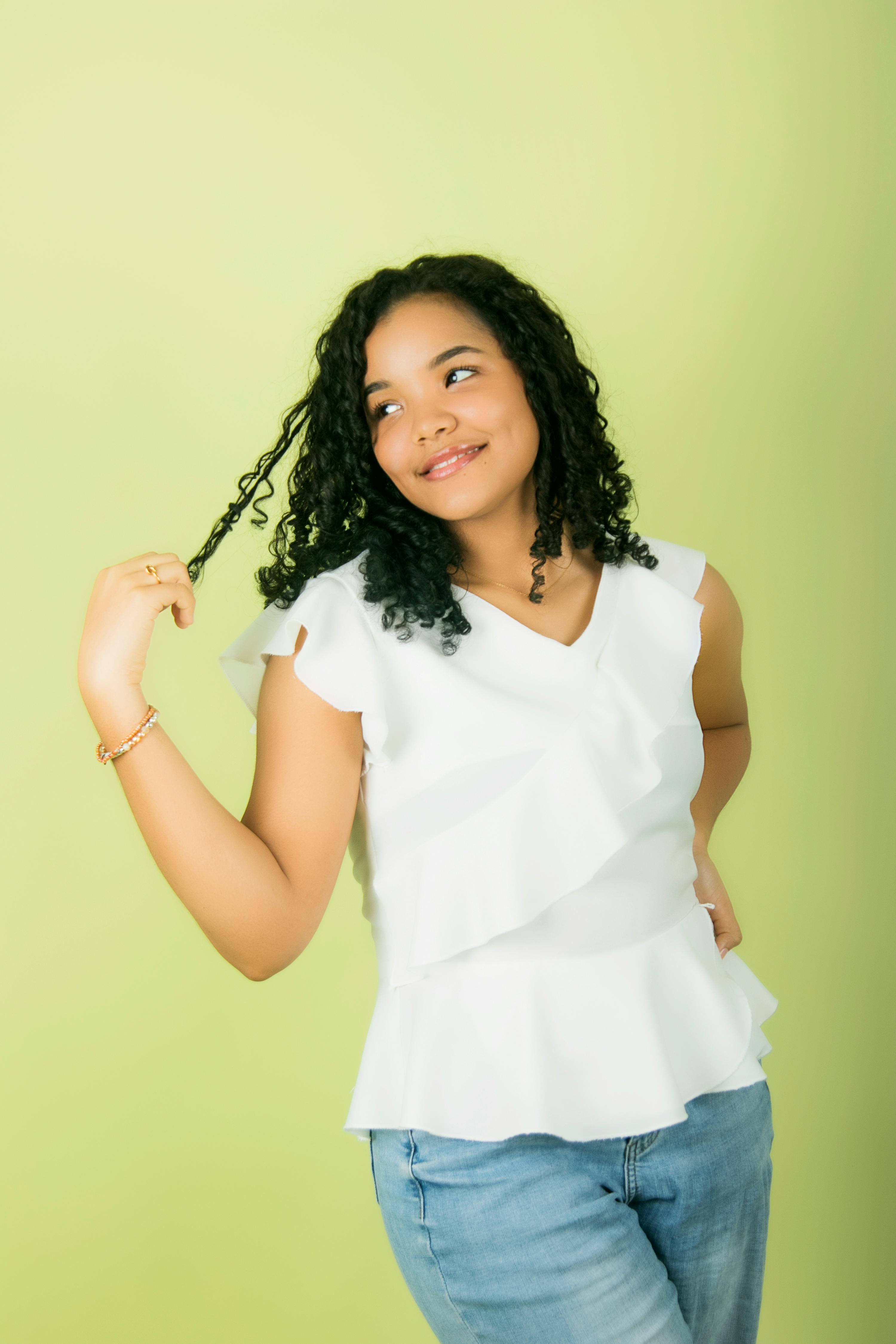 优雅的年轻女子在绿色背景的工作室中，卷发微笑地摆姿势