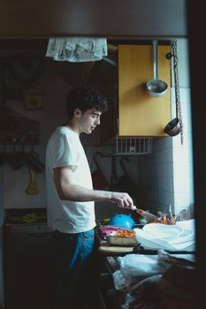 A young man in a casual setting cooking in a cozy home kitchen with utensils around.
