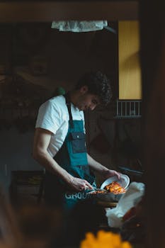 Chef in a dark kitchen preparing a dish with focus and concentration.