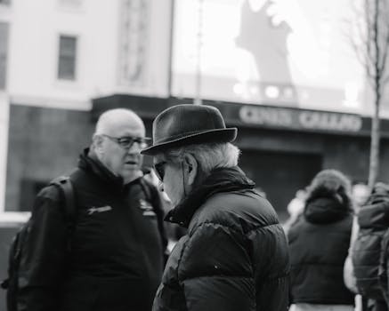 Two elderly men conversing in an urban setting captured in black and white, highlighting city life.