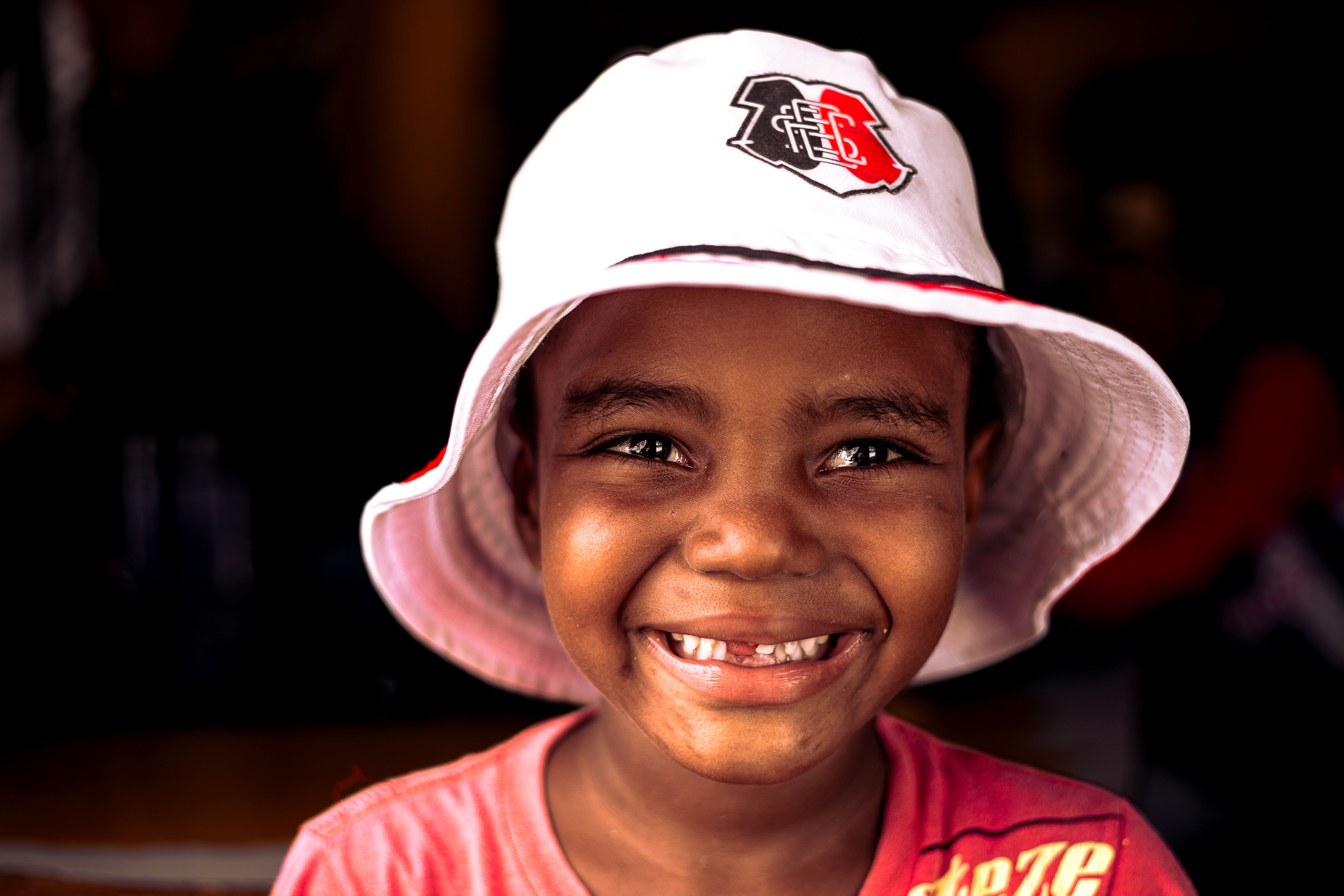 Joyful child with a bucket hat and missing teeth against a black background.