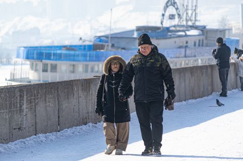 Free Senior couple holding hands on snow-covered urban sidewalk near ship in winter Stock Photo