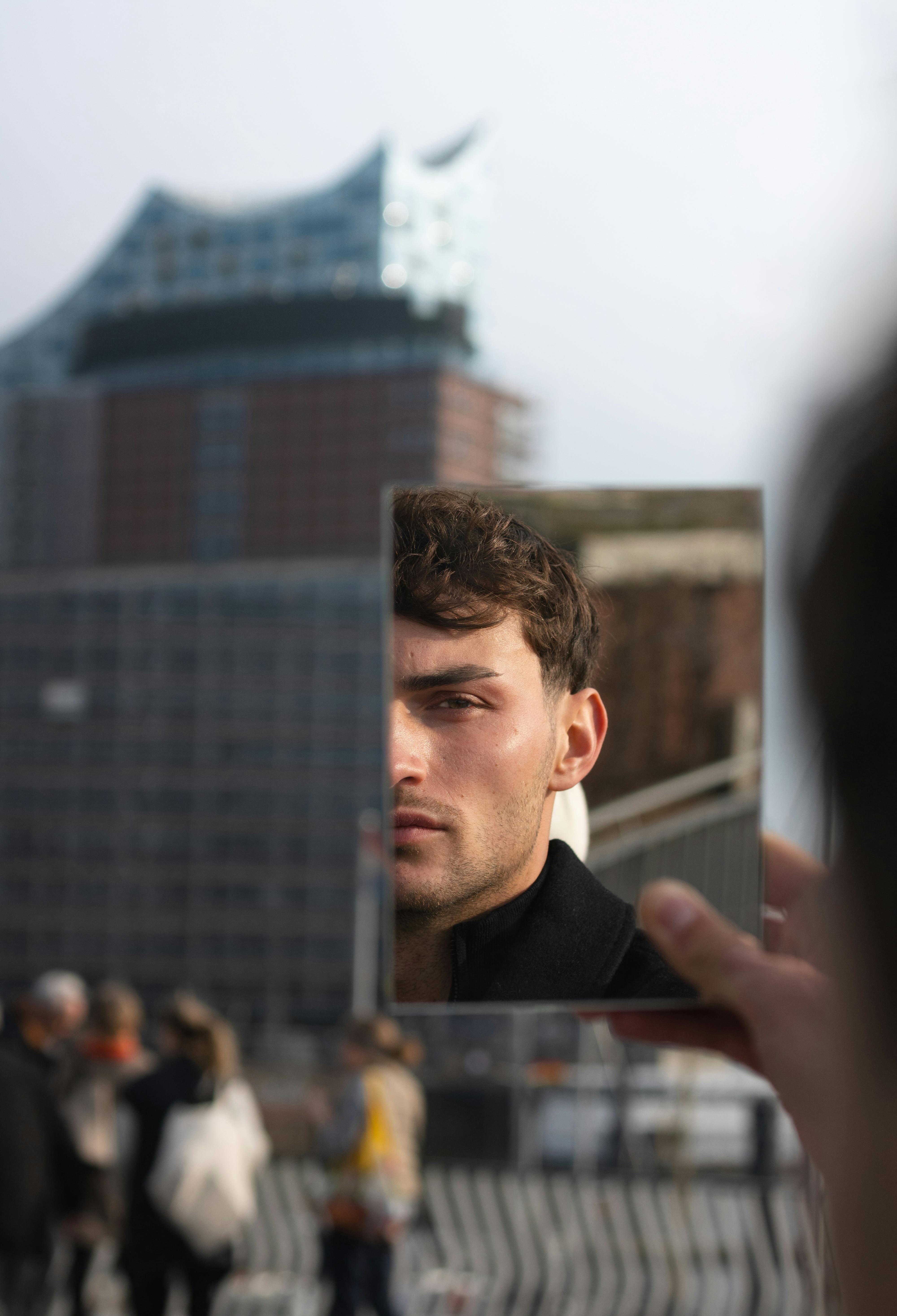 Artistic reflection of a man in a mirror with Hamburg's Elbphilharmonie in the background.