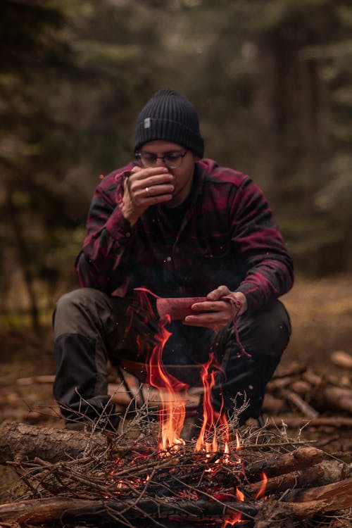 A man sitting by a campfire with a cup of coffee