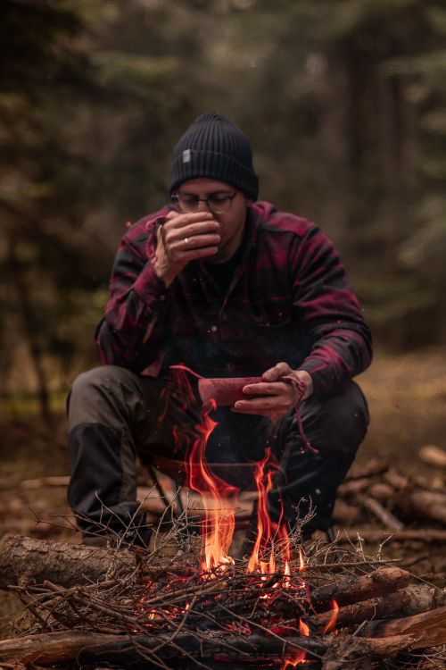 Free A man sits by a bonfire in the forest, enjoying a bowl of stew, creating a warm camping scene. Stock Photo