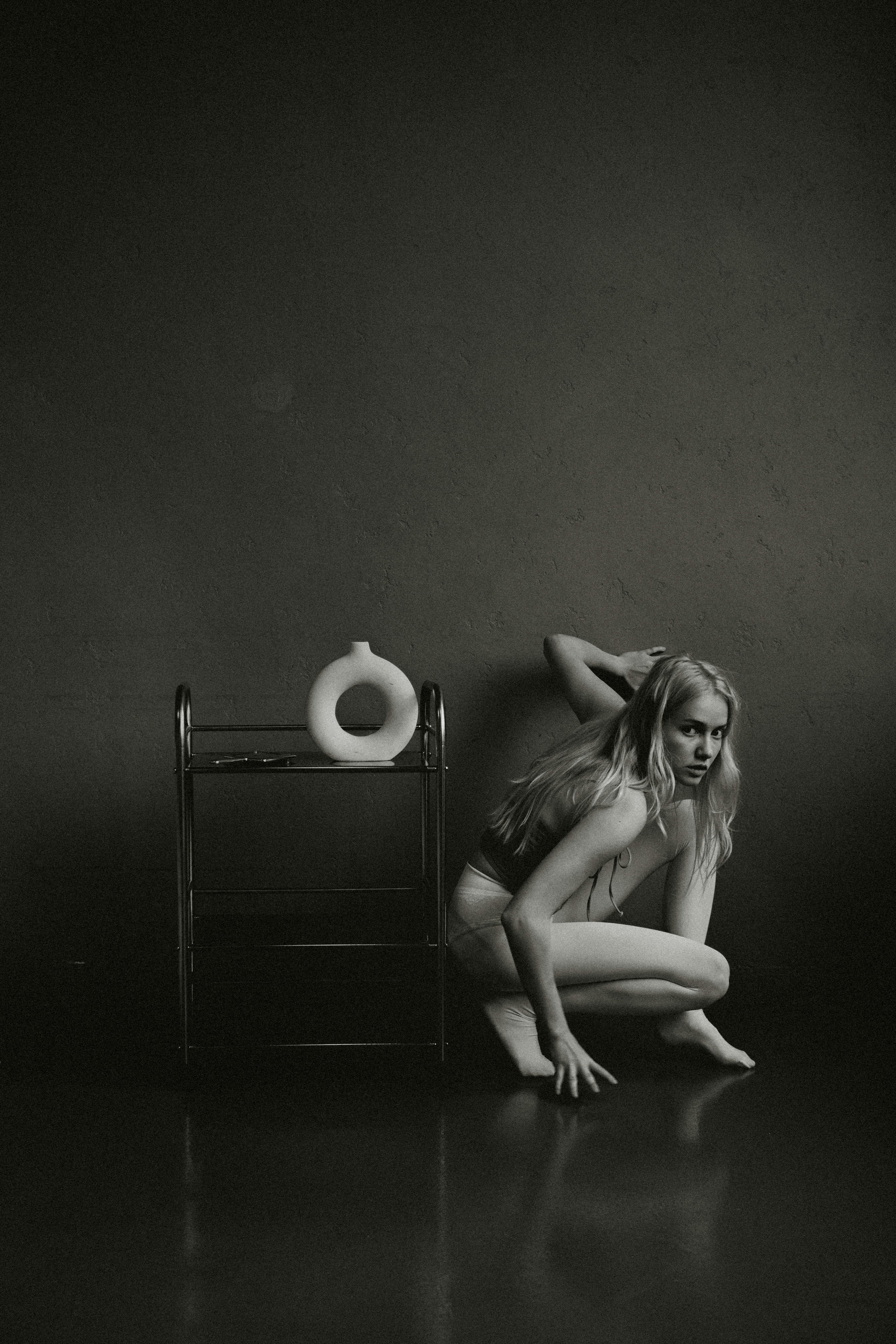 Dramatic black and white image of a woman crouching beside a minimalist setup.