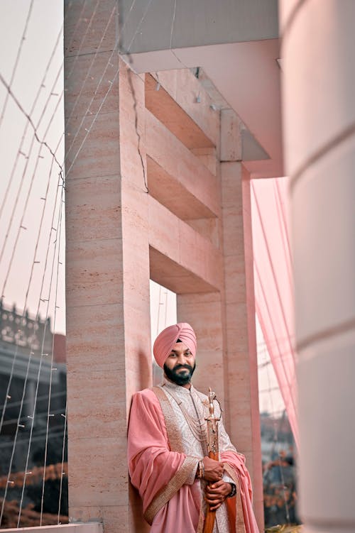 A man in a pink suit and turban standing on a bridge