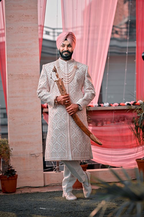 A man in a white turban and pink sherwani holding a sword