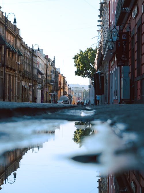 A puddle on the street with buildings in the background