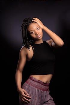 一位扎着辫子的时尚年轻黑人女性，在黑暗背景下自信地摆出姿势，肖像十分迷人