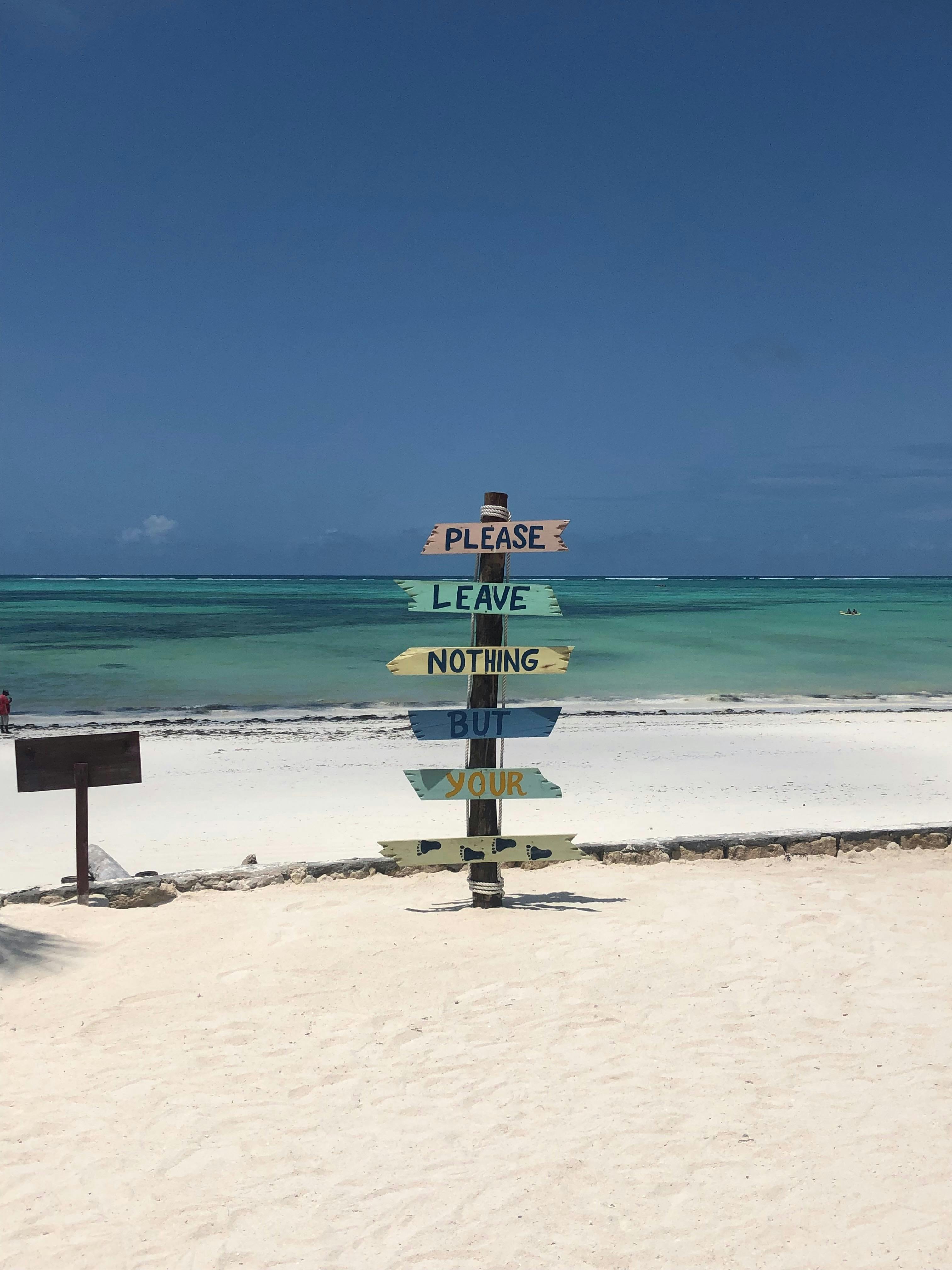 Colorful signpost on a serene Zanzibar beach urging environmental care.