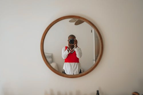 Woman in Red Top and White Shirt Taking Selfie in Round Mirror on Wall
