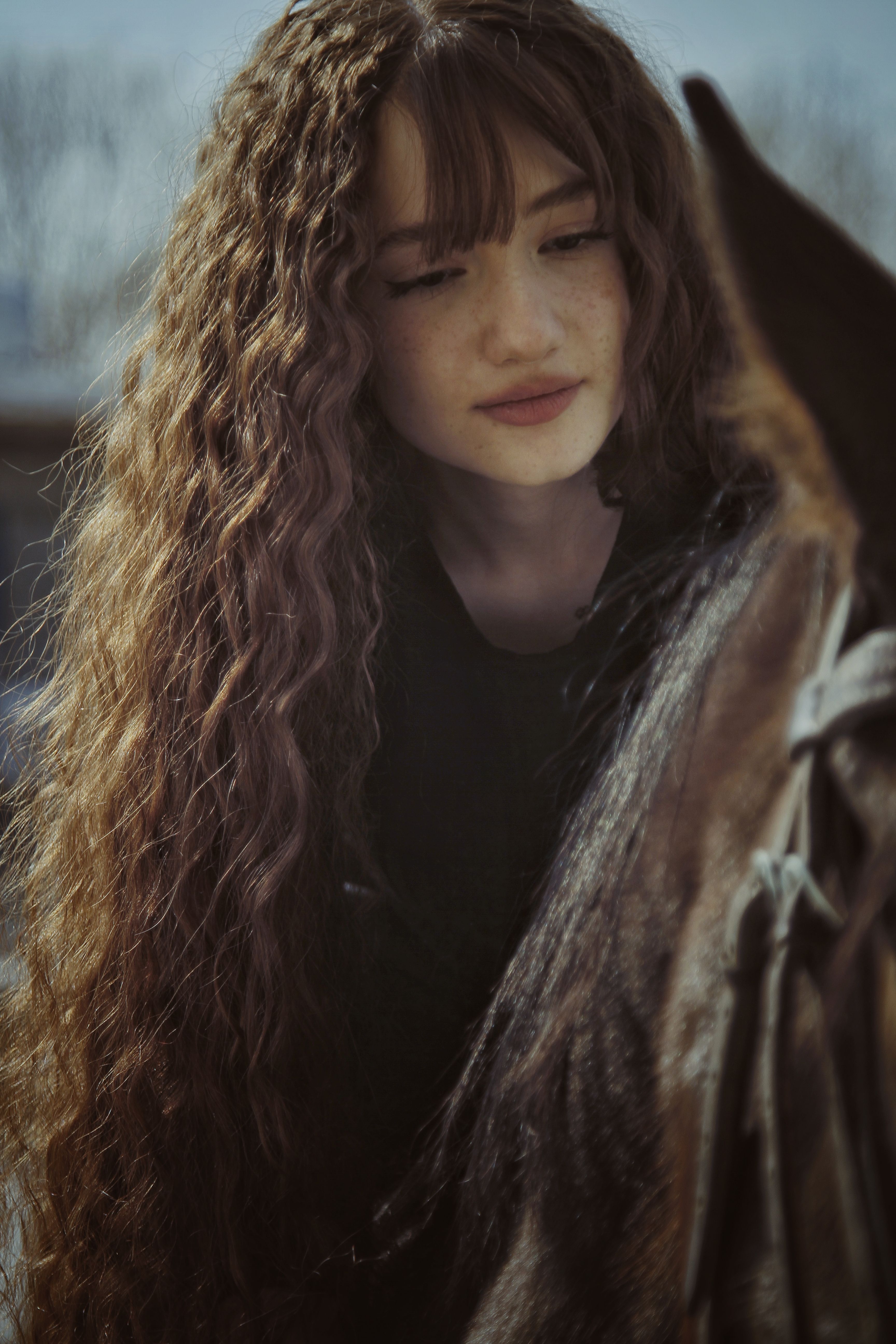 A serene portrait of a young woman with long wavy hair and freckles, softly lit.
