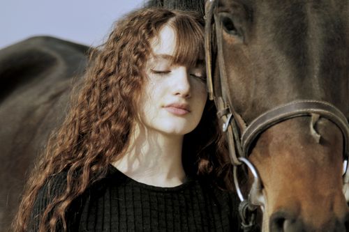 Free A young woman with curly hair shares a serene moment with a horse outdoors, evoking tranquility and connection. Stock Photo