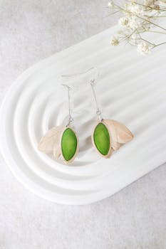 Leaf-shaped earrings with green stones displayed on a white textured tray.