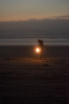 Silhouette walking with lantern on beach at dusk, creating a mysterious mood.
