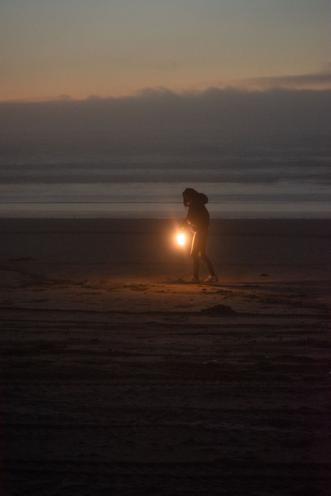 Person carrying a light along a beach at sunset
