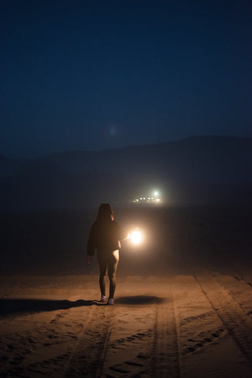 A person walking on a beach at night with a flashlight