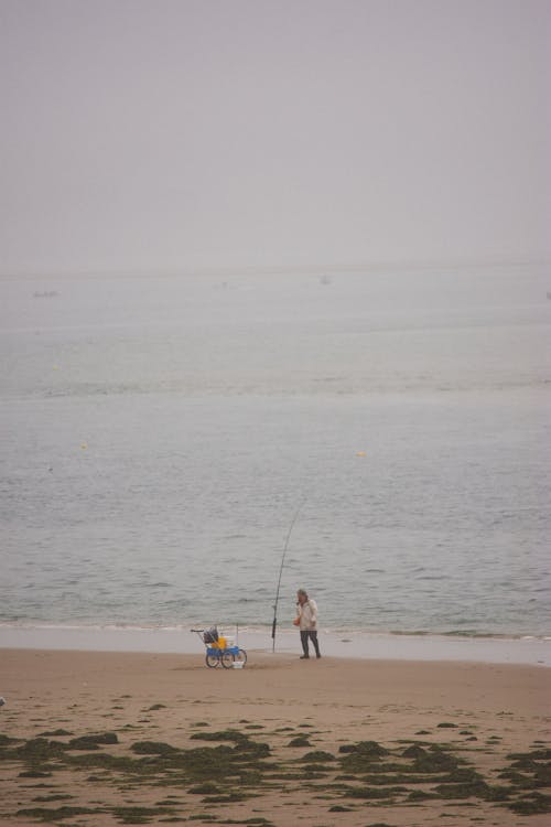 A person is standing on the beach with a fishing pole