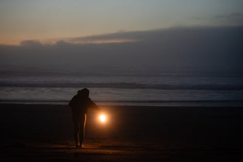 A person holding a lantern on the beach at night