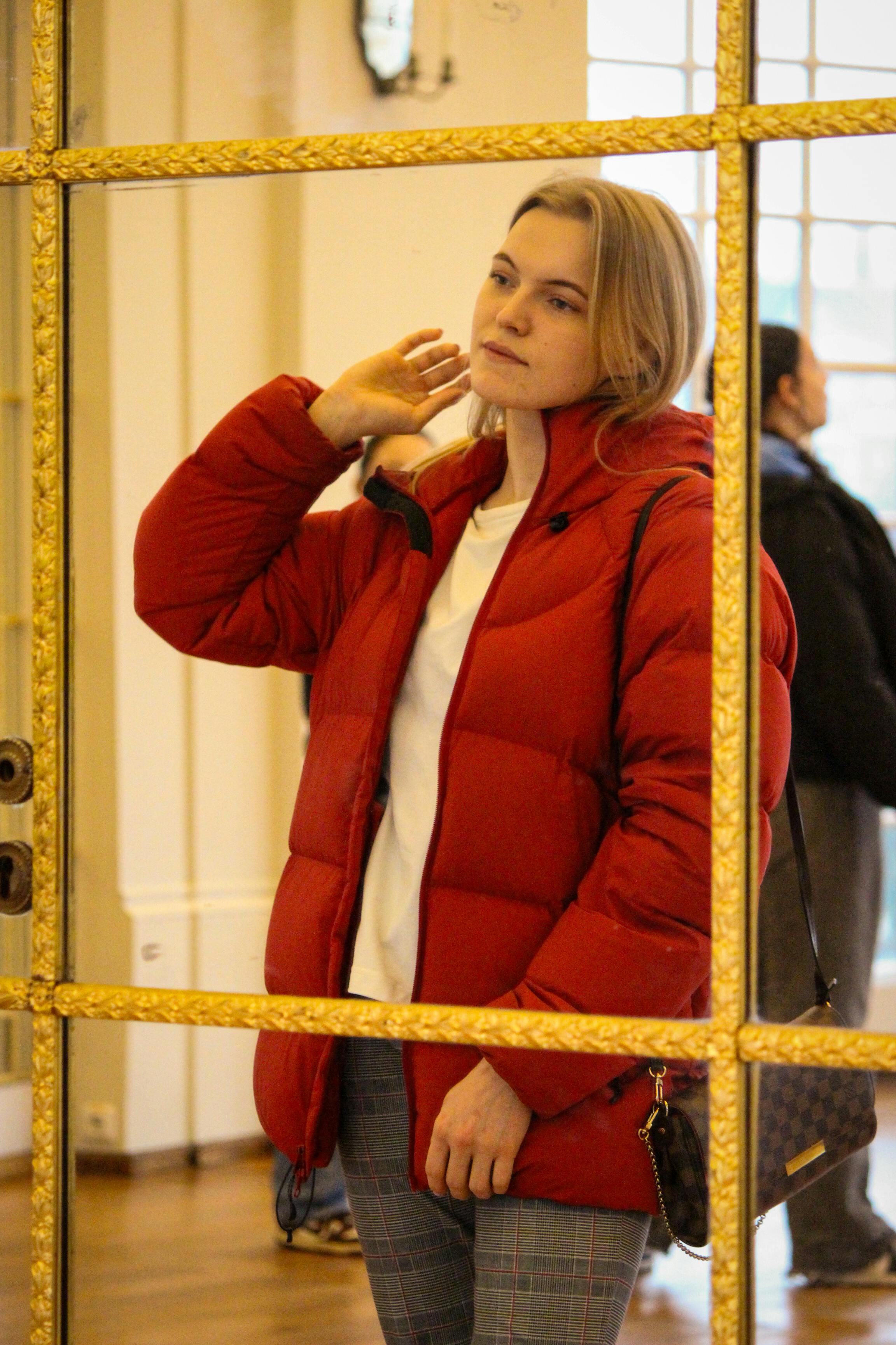 blonde woman in red puffer jacket looking at mirror