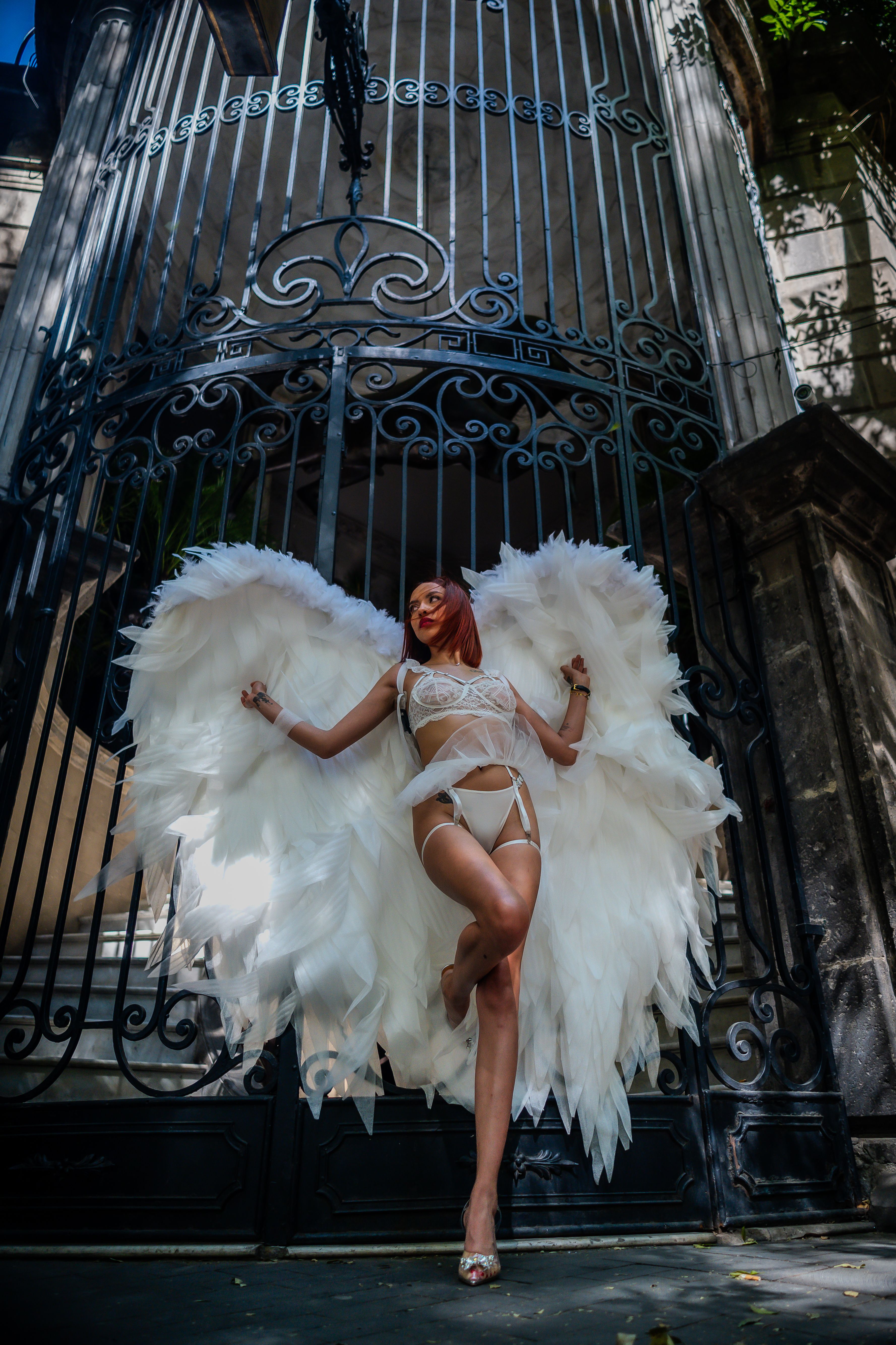 A woman in an elaborate angel costume poses confidently against a wrought iron gate in Ciudad de México.