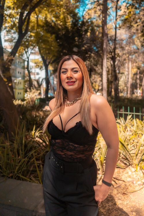 Free Stylish woman in a lace top poses confidently outdoors in a sunlit park. Stock Photo