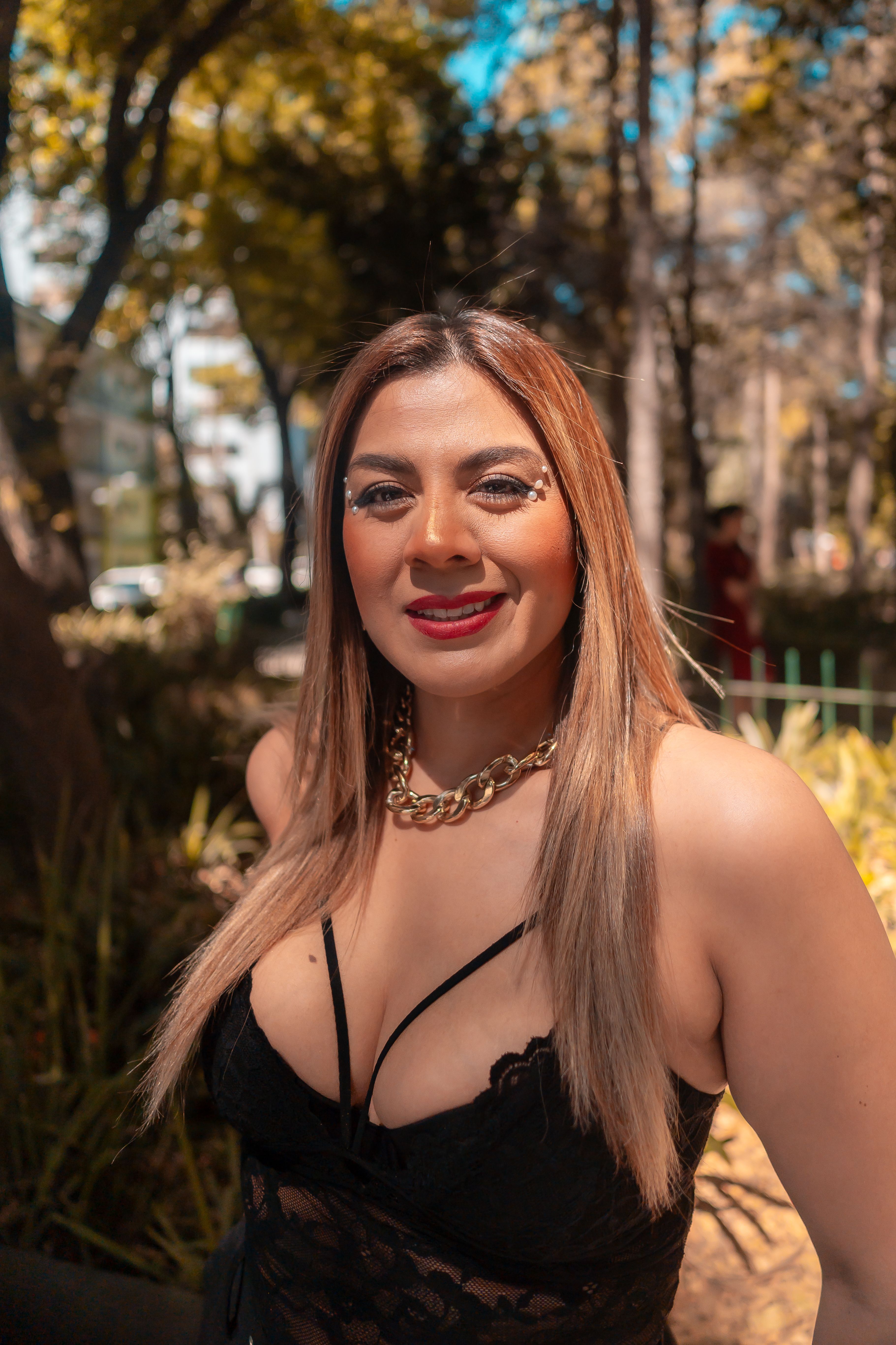 Portrait of a fashionable woman in a park, showcasing glam style under bright sunlight.