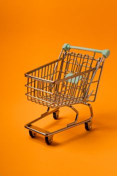 A miniature shopping cart set against a bold orange backdrop, ideal for marketing and business visuals.