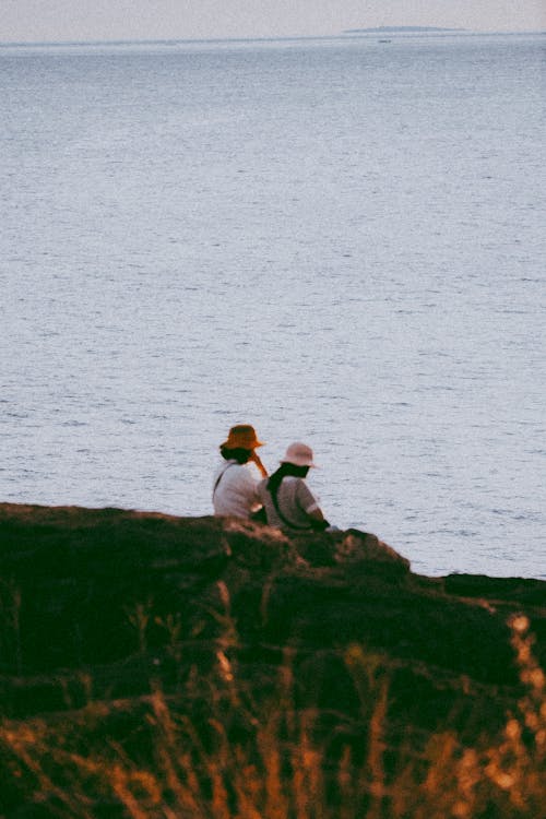 Back View of People Sitting on a Cliff at Seashore