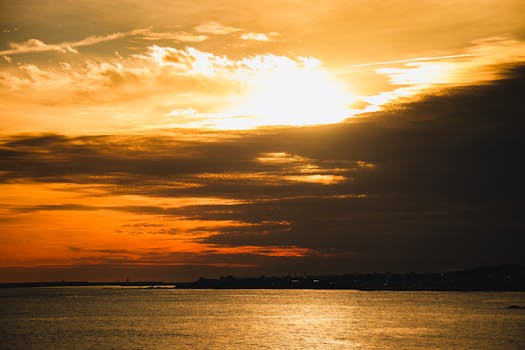 A stunning sunset with vivid orange skies over a calm sea, offering a serene coastal view.