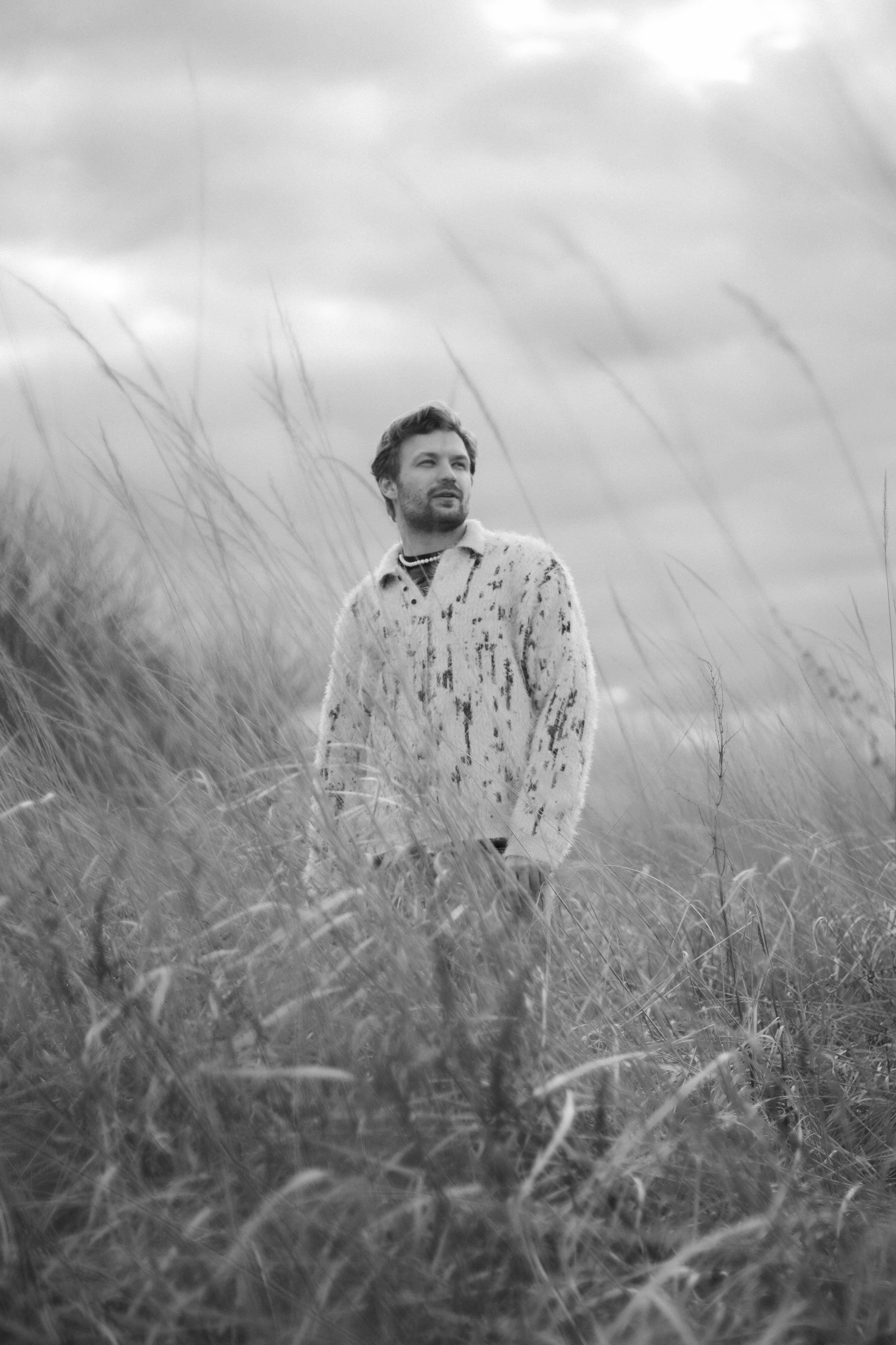Captivating black and white portrait of a man standing in a rural grassland.