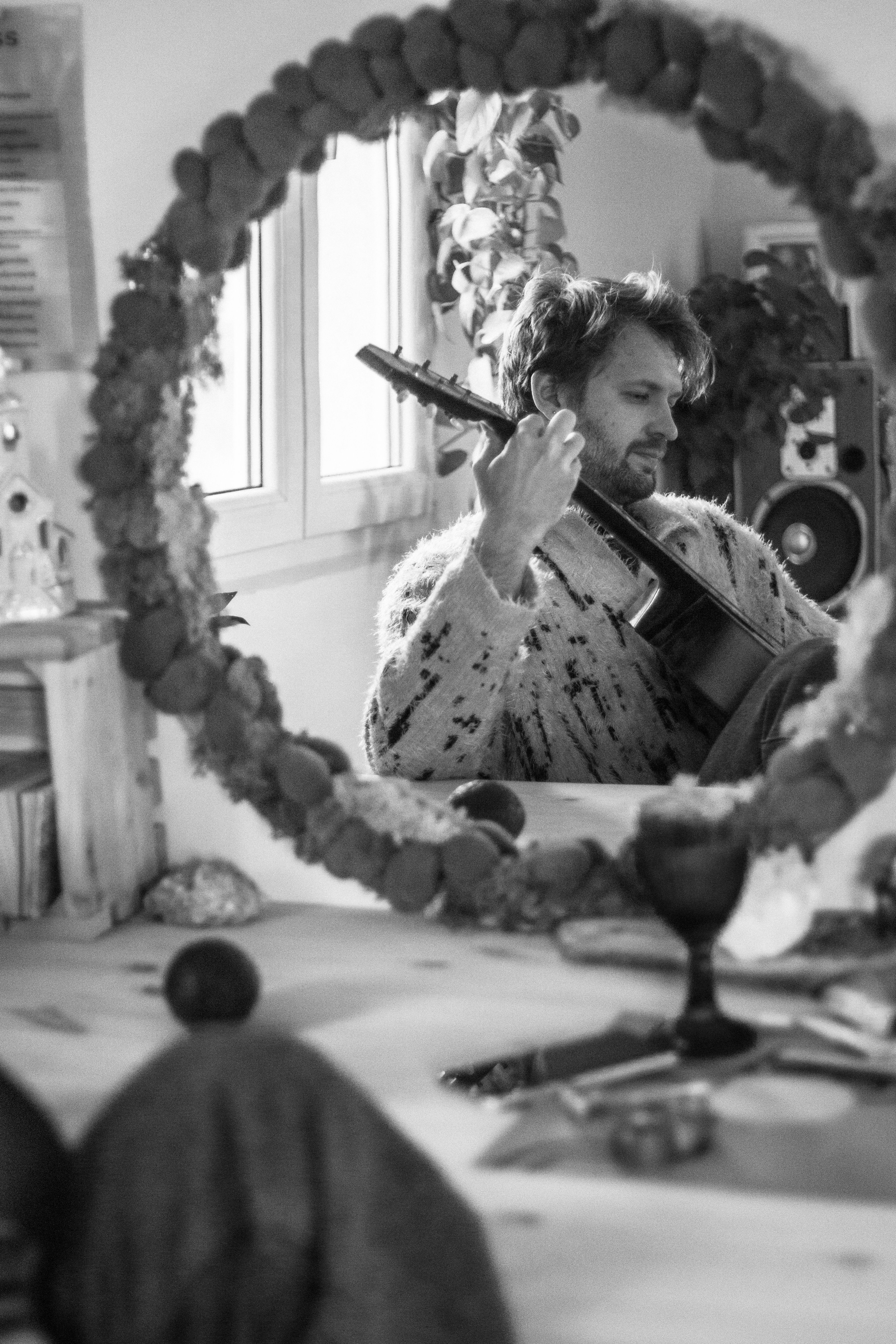 Reflection of a man holding a guitar in a cozy indoor setting.