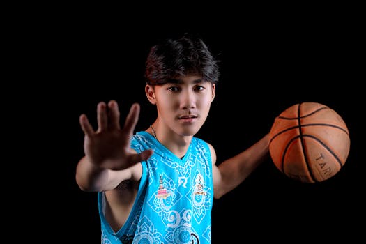 Dynamic portrait of a young basketball player in sportswear on black background.