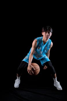 A young Asian male athlete dribbling a basketball in a blue uniform during a studio session.