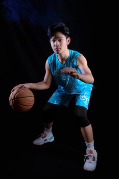 Young basketball player dribbling a ball in sportswear against a dark backdrop. Action shot.
