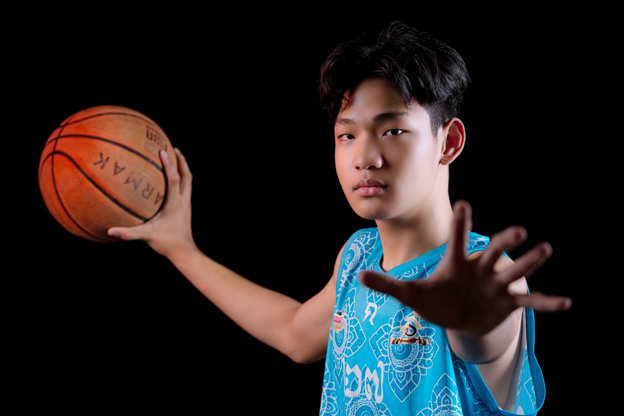 teenager in blue jersey posing with a basketball against black backdro