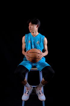 A young male basketball player in blue sportswear holds a ball in a studio setting.