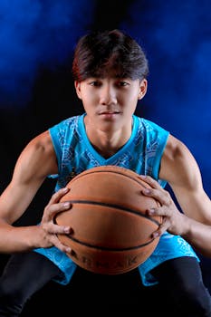 Energetic portrait of a young male athlete holding a basketball in a dynamic studio setup.
