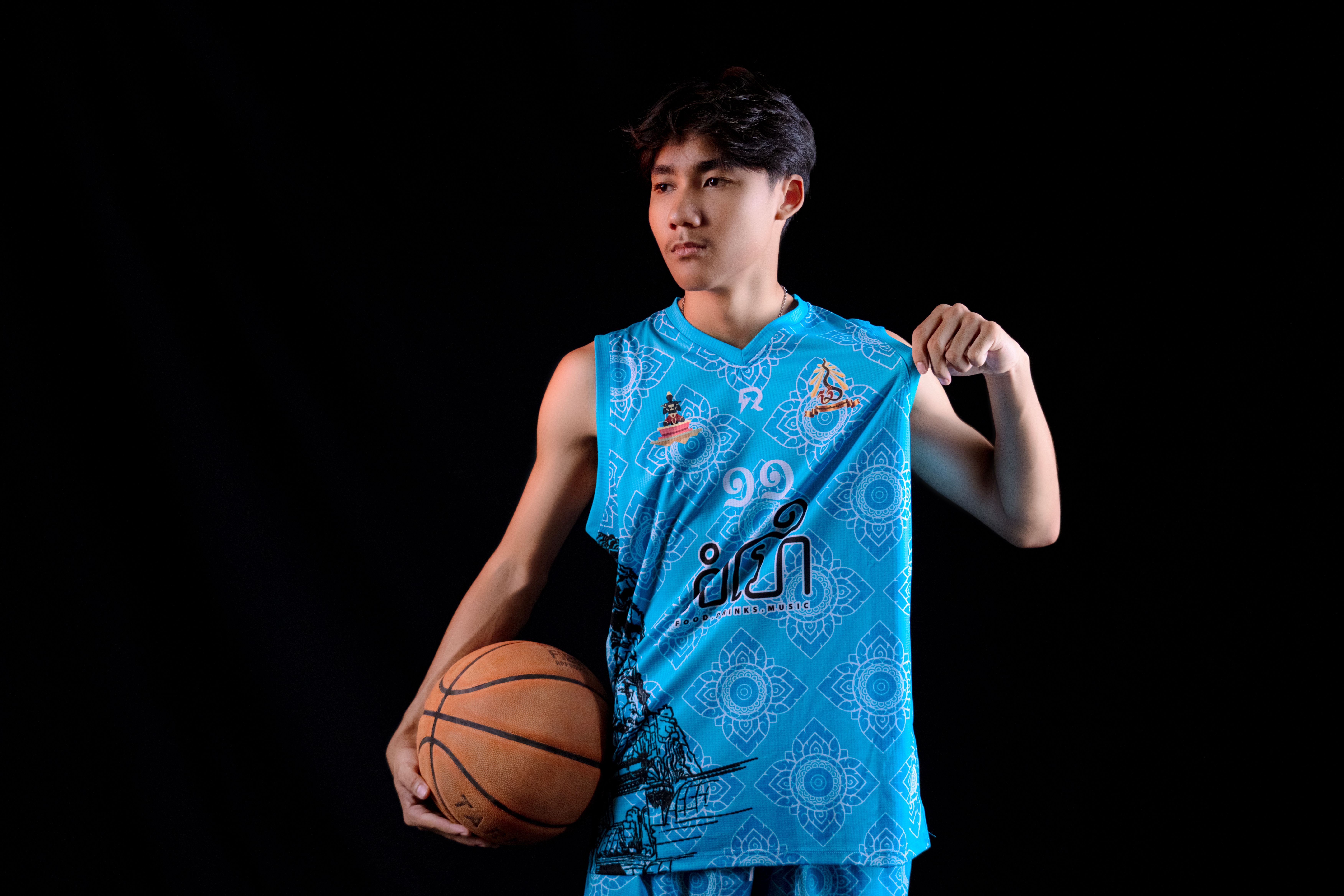 Young Asian basketball player in blue jersey posing in a studio with a black background.