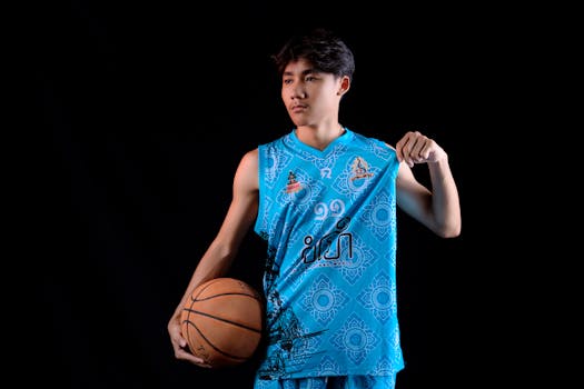 Young Asian basketball player in blue jersey posing in a studio with a black background.