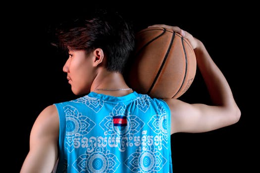 Muscular male basketball player in sportswear, holding a ball against a dark background.