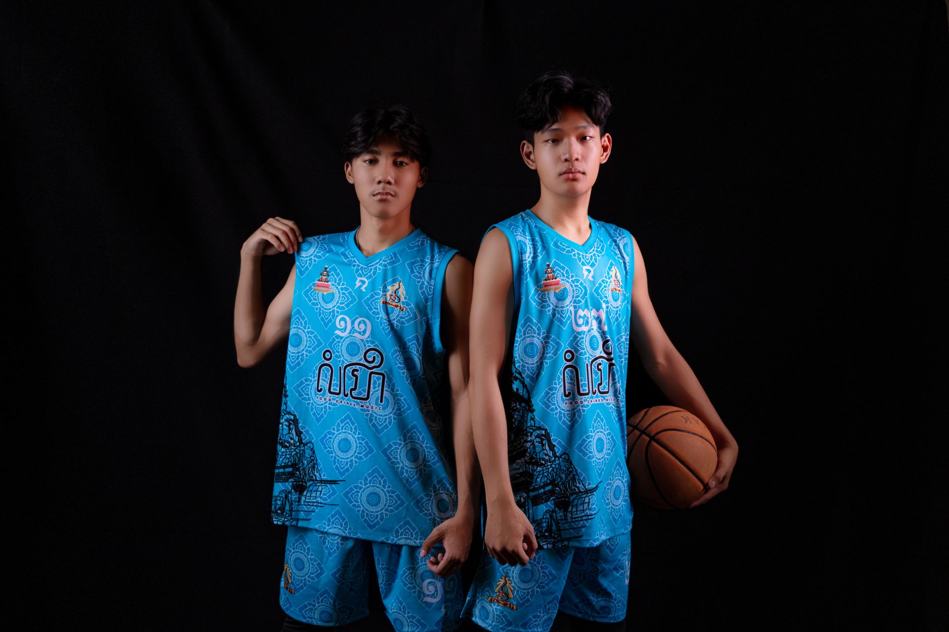 Studio photo of young Asian men in blue basketball uniforms holding a ball, showcasing team spirit.