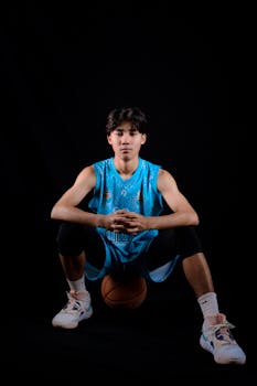 Studio portrait of a focused teenage basketball player in a blue jersey against a black background.