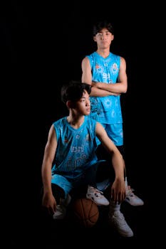 Two teenage basketball players pose confidently in a studio with a dark backdrop.