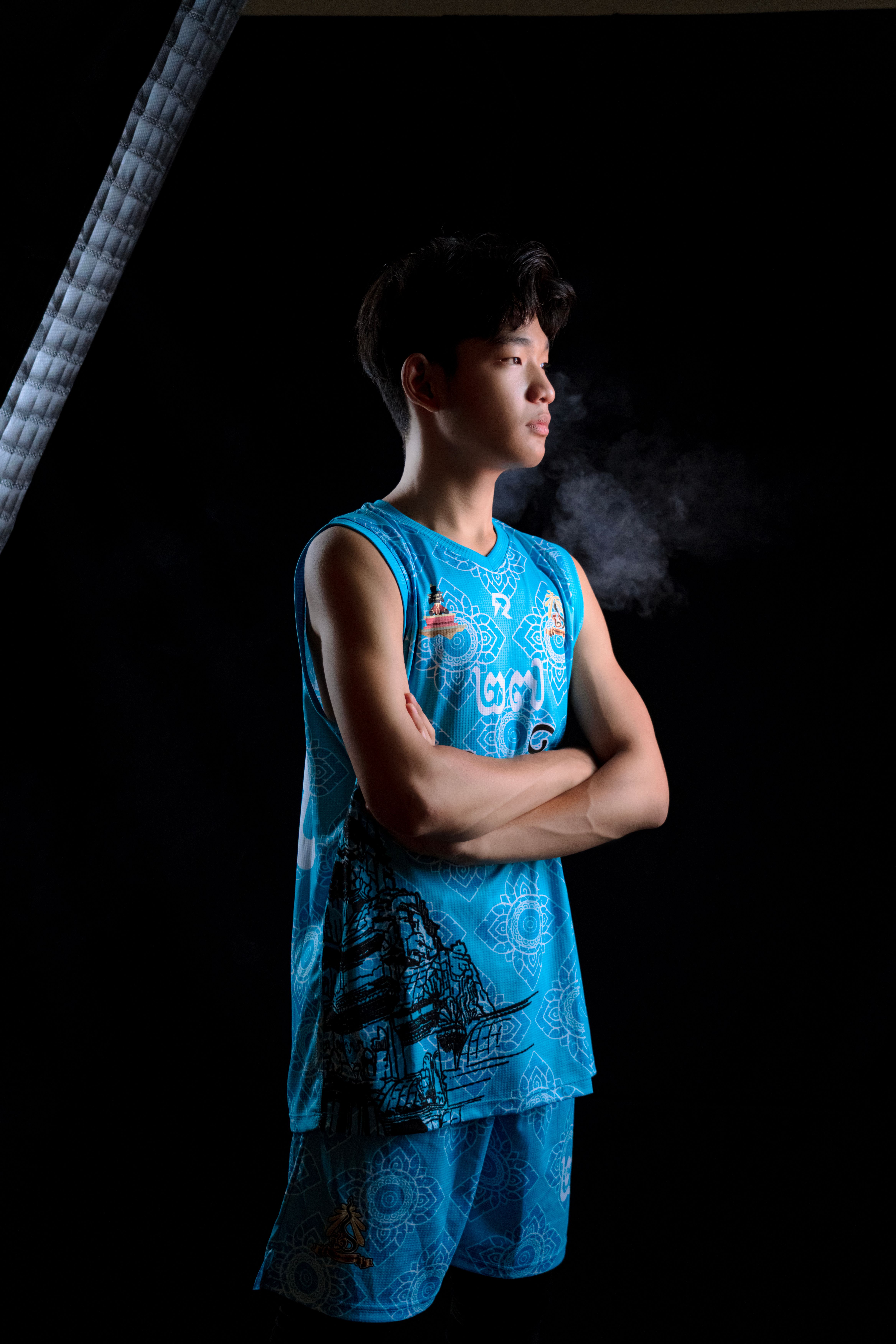 Confident young basketball player poses in vibrant sportswear against a dark backdrop.